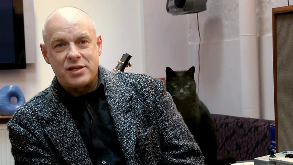 It's a photo of Angel the cat staring menacingly from behind Brian Eno's shoulder.